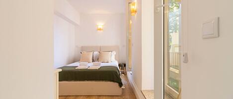 A bedroom with a bed, pillows, a green blanket, and a nightstand. There is a sliding glass door leading to an outdoor area.