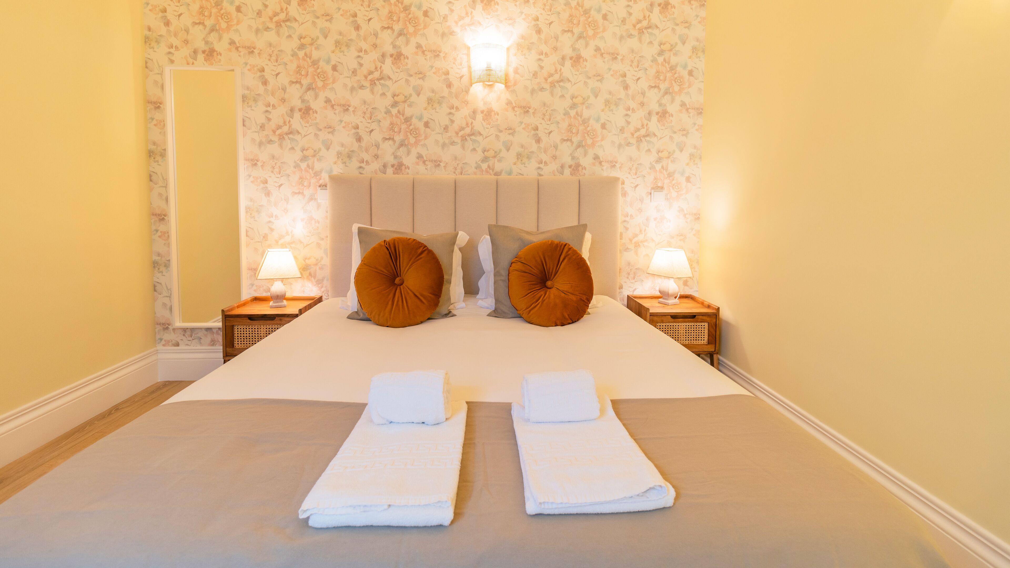 Una cama bien hecha con dos almohadas, dos mesitas de noche con lámparas y un papel tapiz floral.