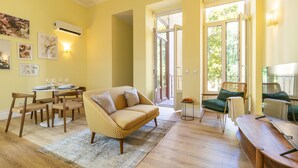 Ein Wohnzimmer mit einer Couch, Sesseln, einem Esstisch mit Gläsern und Blick durch eine Glastür.