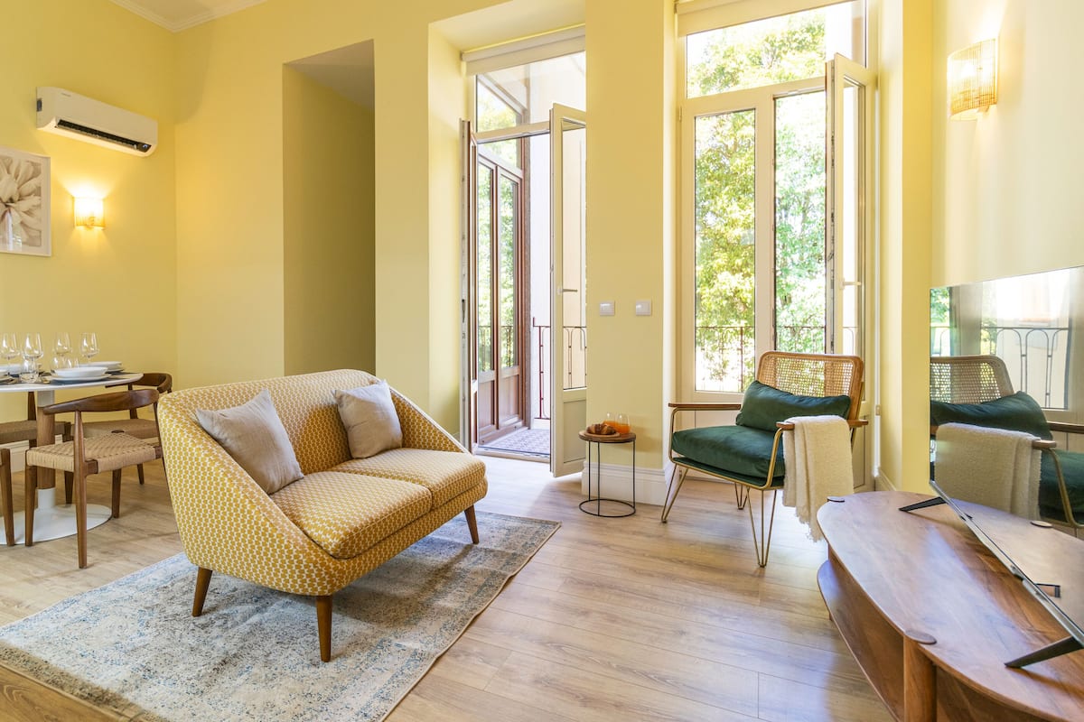 A living room with a sofa, chairs, a dining table with glasses, and a view through a glass door.
