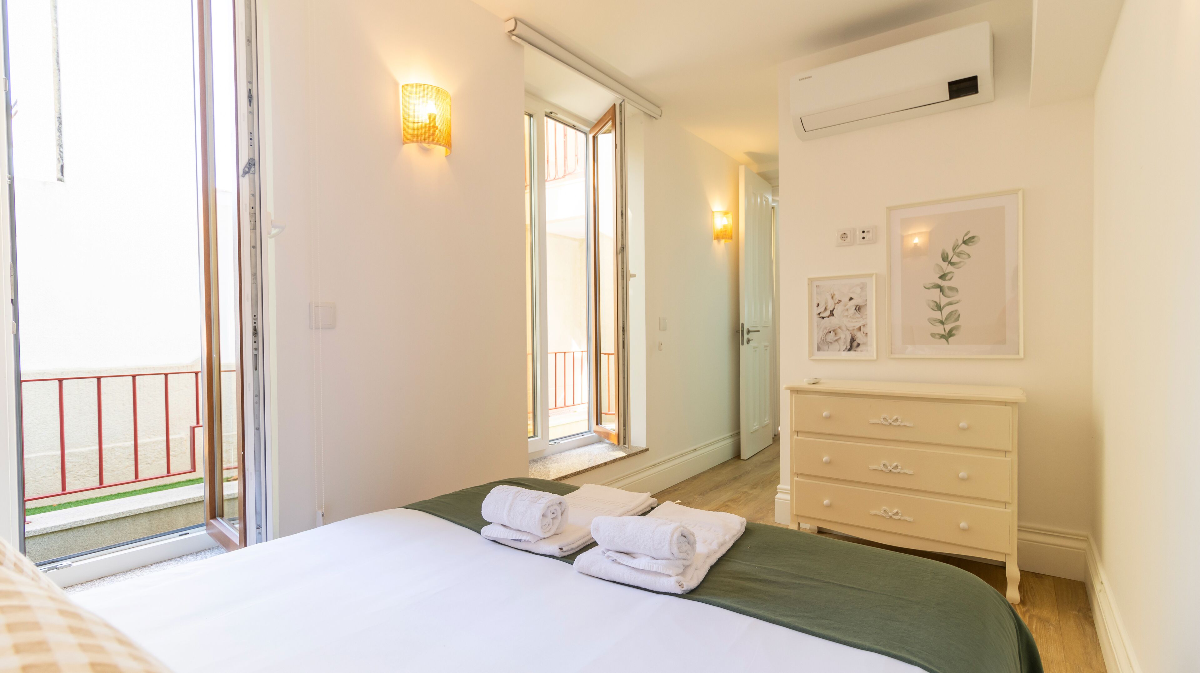 A bedroom with a bed, a dresser, a mirror, and a balcony.