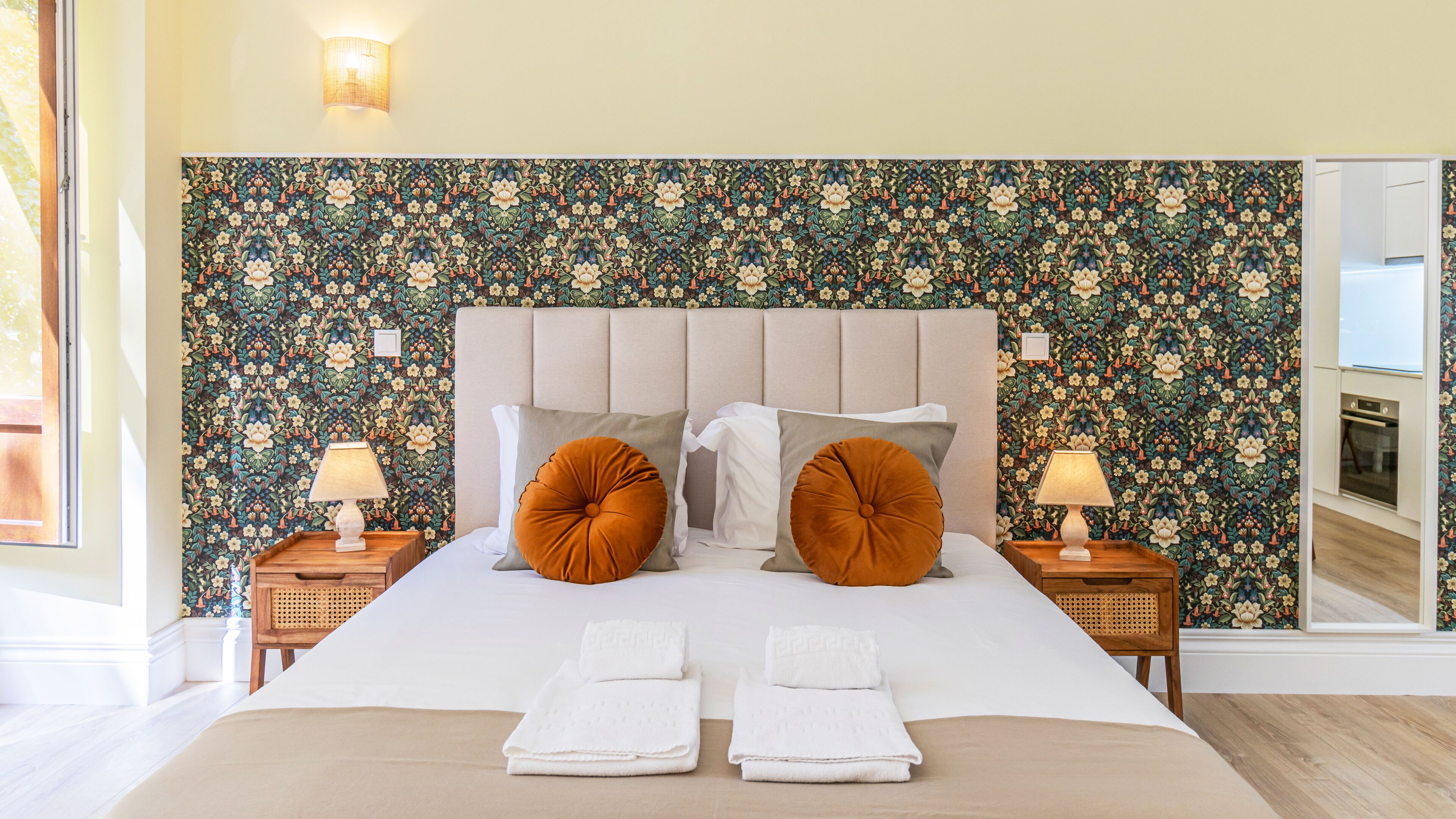 A hotel room with a large bed, two nightstands, a headboard, and a floral wallpaper.