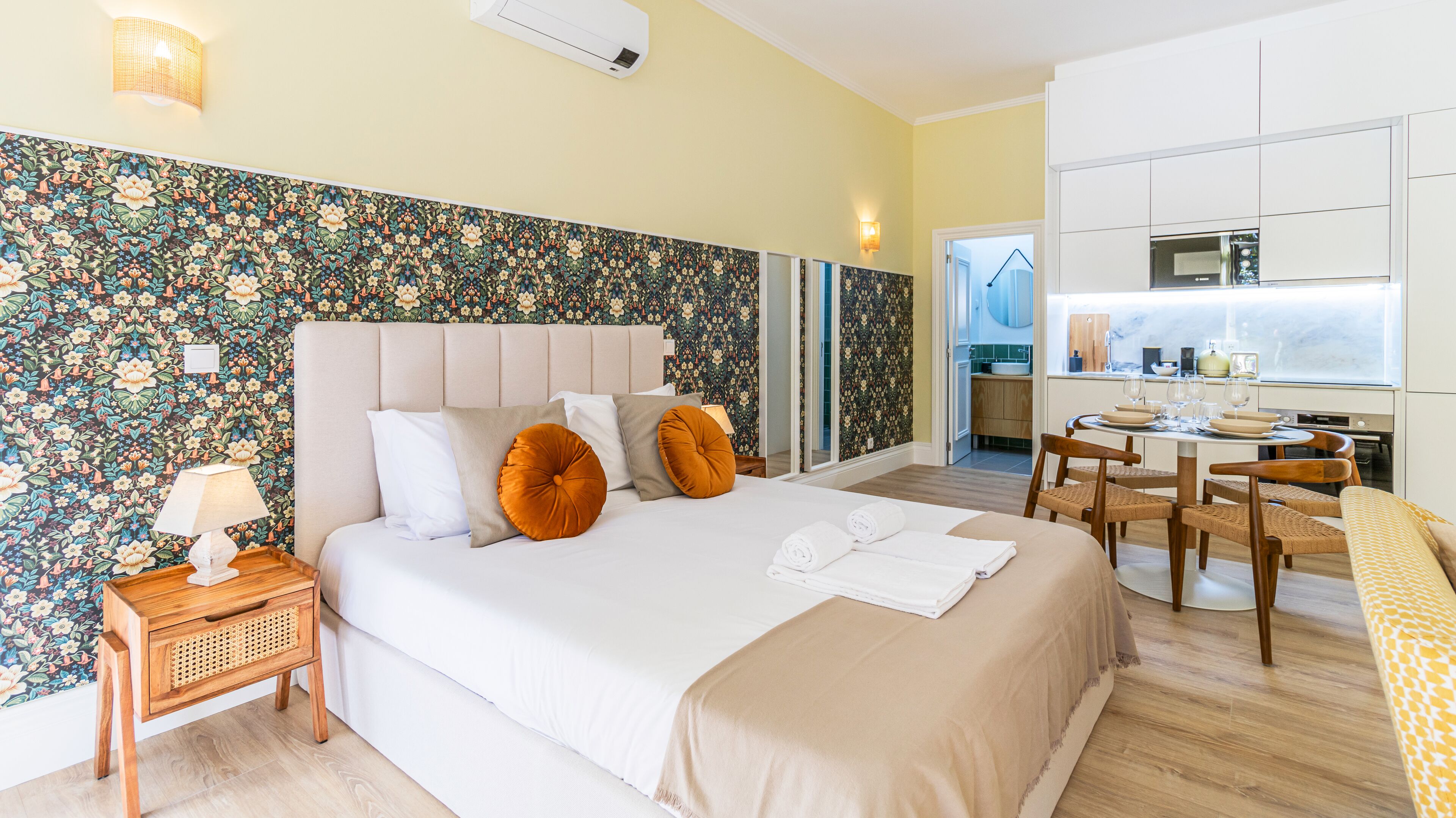 Une chambre d’hôtel avec un grand lit, une table de chevet avec une lampe, une commode en bois et une vue sur la cuisine.