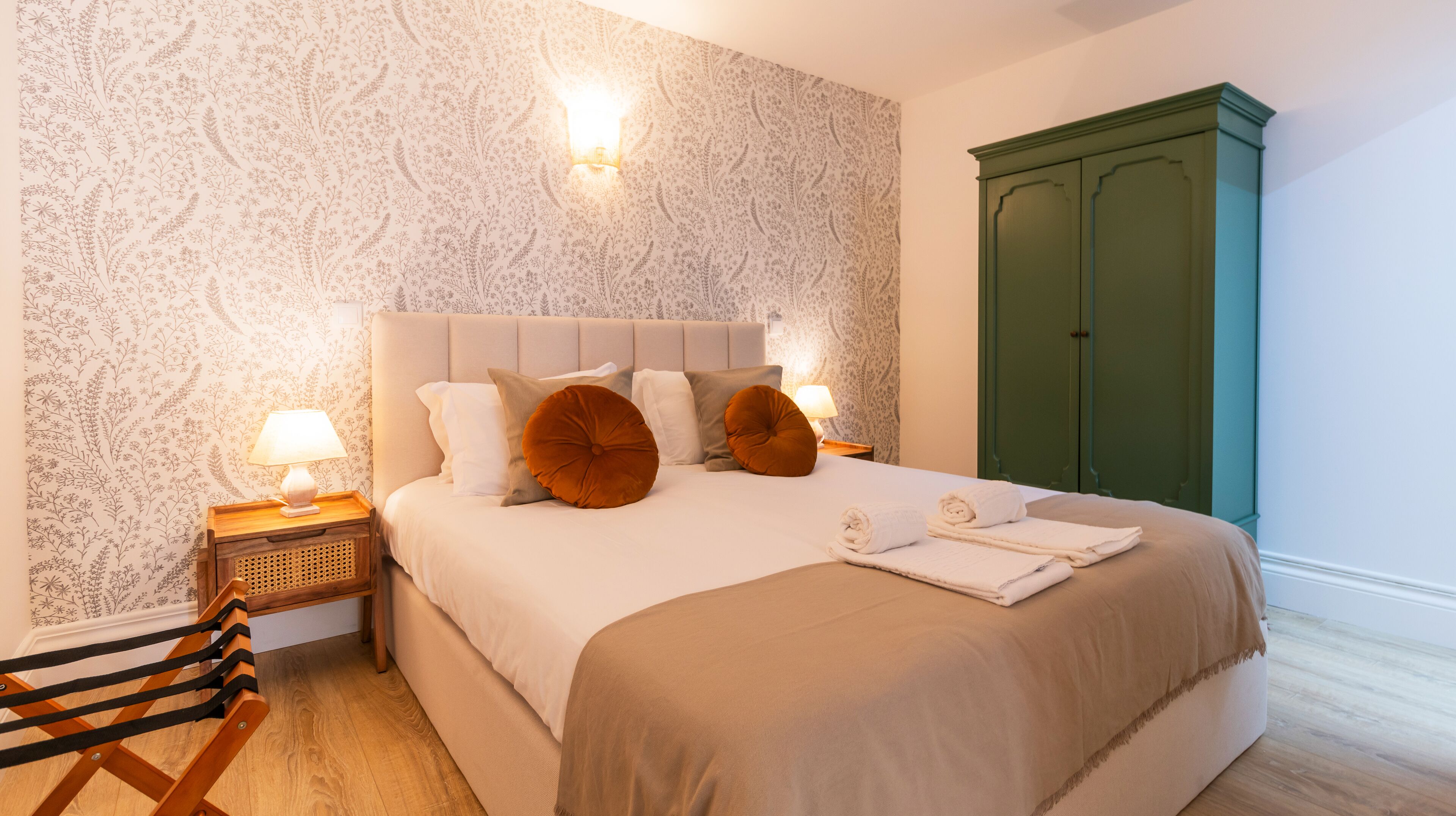 Een net opgemaakt bed met hoofdbord, twee bedlampjes en een groene garderobe.