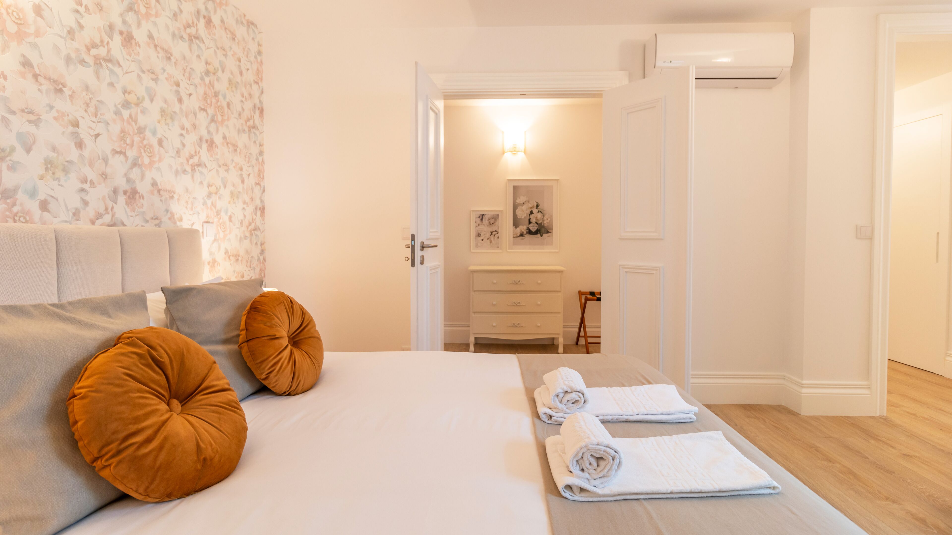 A bedroom with a bed, pillows, a nightstand, a dresser, and a door leading to another room.