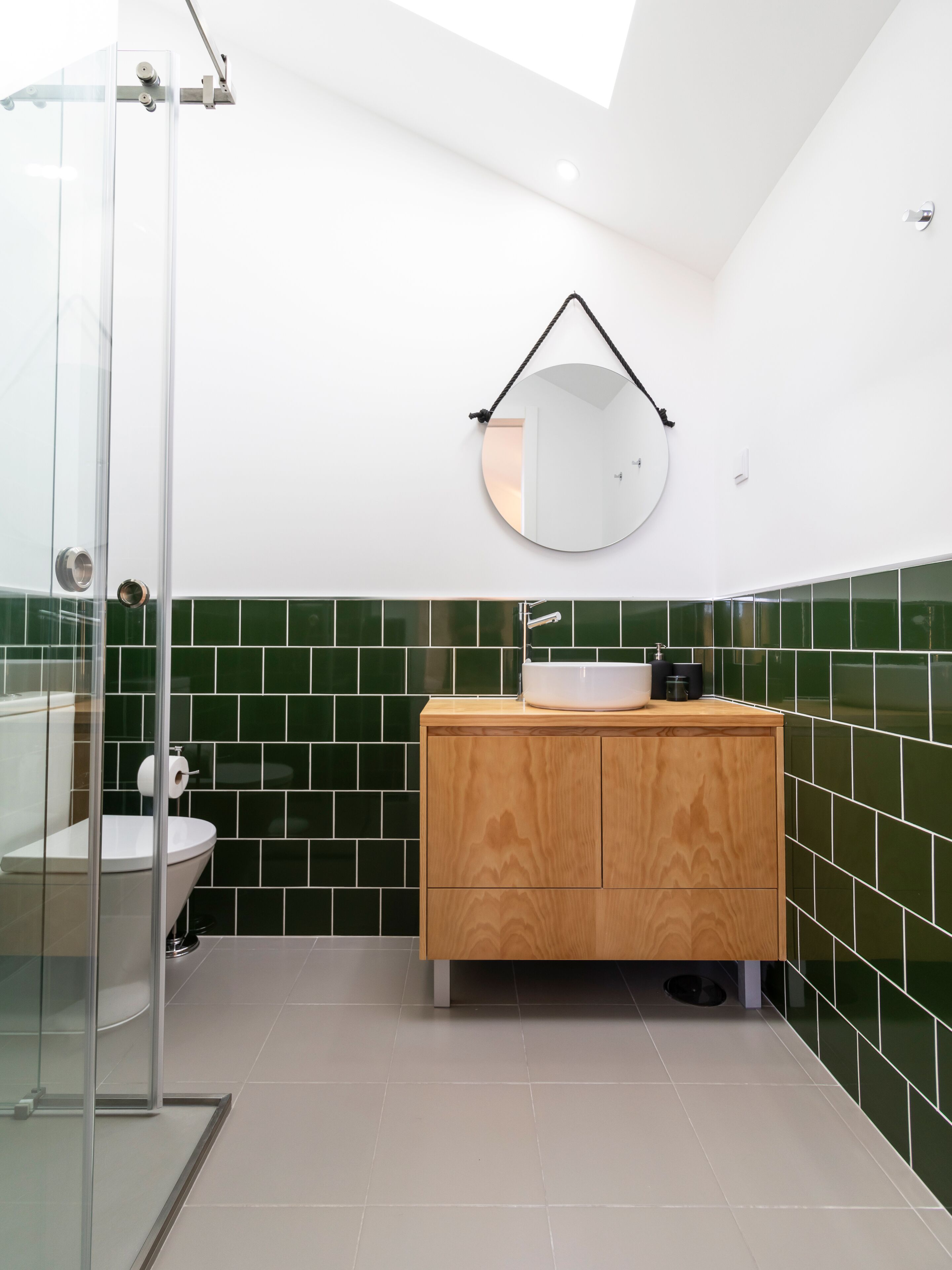 A modern bathroom with a glass shower enclosure, a wooden vanity with a sink, and green-tiled walls.