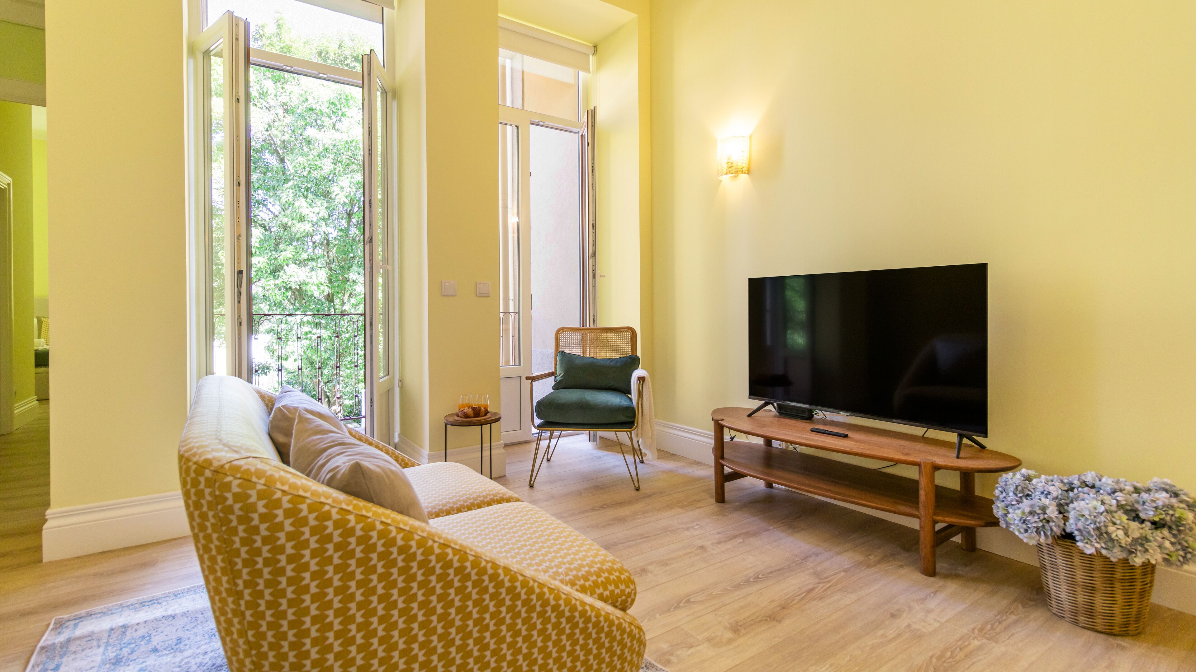 A living room with a sofa, a chair, a TV, and a window with a view of trees.