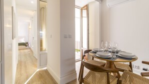 Ein moderner Essbereich mit einem runden Tisch für vier Personen, Korbstühle und Blick auf einen Balkon durch eine Glastür.