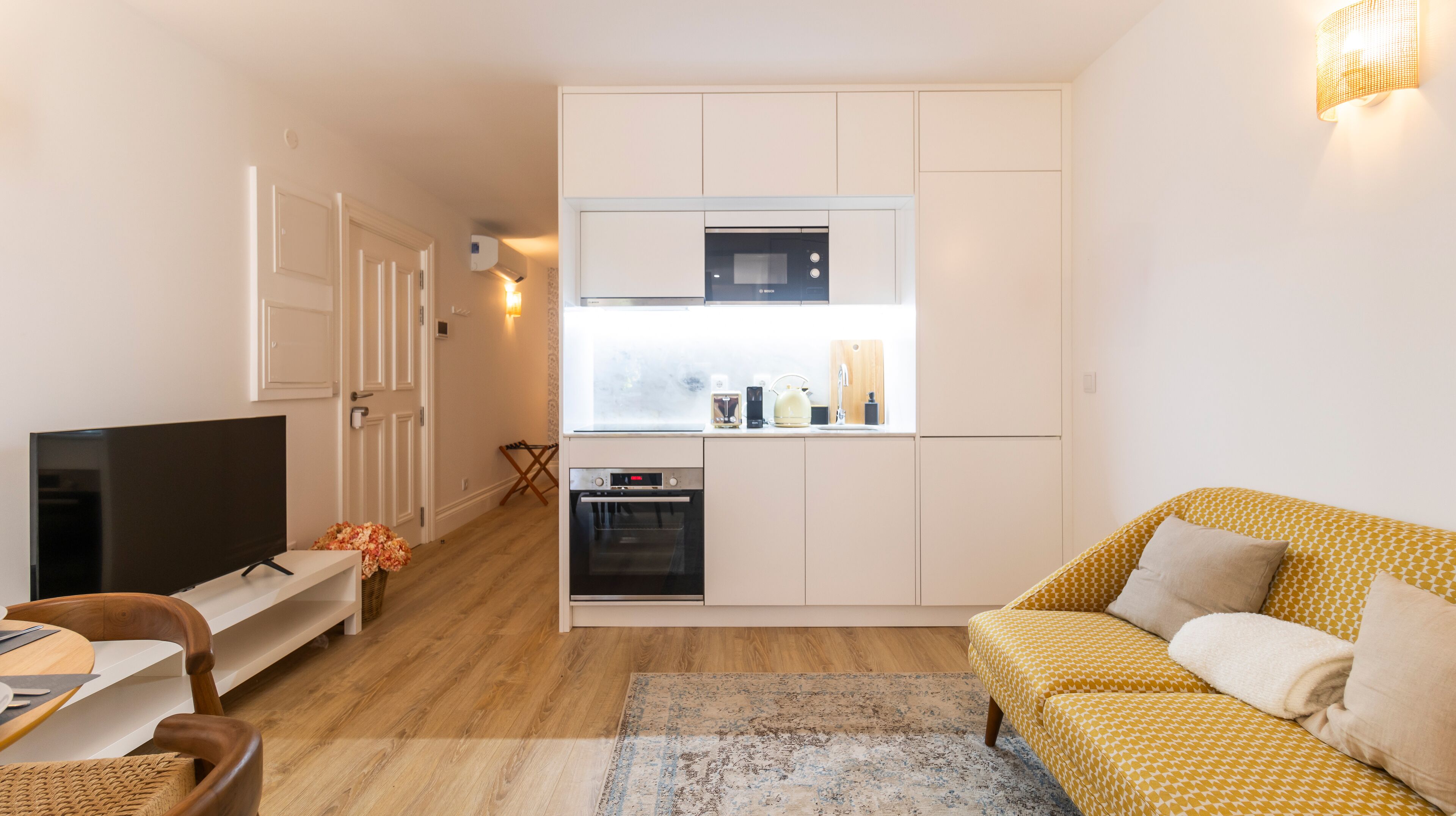 A compact living space with a kitchenette, a flat-screen TV, a sofa, and a dining area.