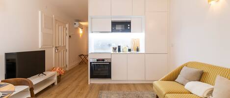 A compact living space with a kitchenette, a flat-screen TV, a sofa, and a dining area.