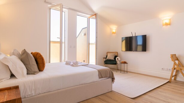 Ein modernes Schlafzimmer mit einem großen Bett, einem Flachbildfernseher und Blick ins Freie.