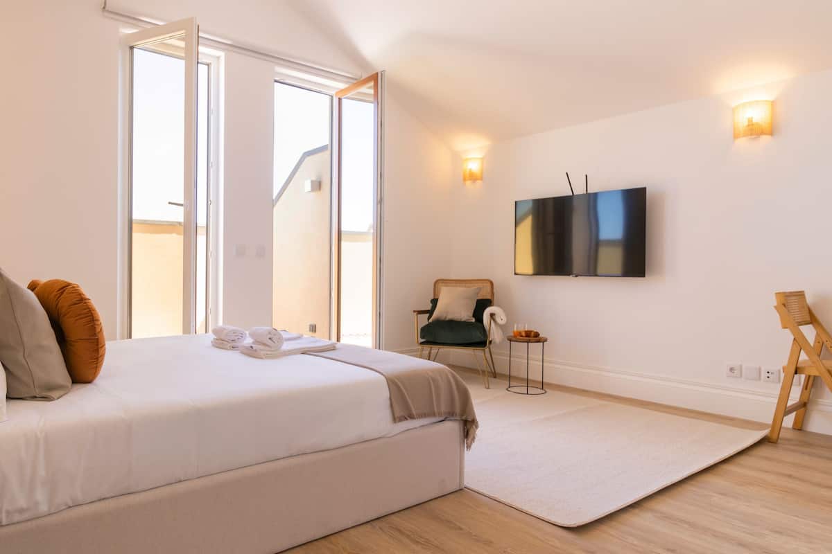 A modern bedroom with a large bed, a flat-screen TV, and a view of the outdoors.