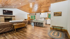 A spacious living area with a fireplace, a sofa, a coffee table, and a dining table with chairs. There is a kitchen area with white cabinets and a large island. - Blueberry: 3  BR, 3  BA House in Canaan Valley, Sleeps 6 (Canaan Valley)