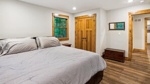 A bedroom with a bed, a window with a view of trees, a wooden wardrobe, a small table, and a mirror on the wall. - Blueberry: 3  BR, 3  BA House in Canaan Valley, Sleeps 6 (Canaan Valley)