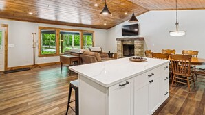 A spacious living area with a large wooden ceiling, a stone fireplace, a white kitchen island, and a dining area with wooden chairs. - Blueberry: 3  BR, 3  BA House in Canaan Valley, Sleeps 6 (Canaan Valley)