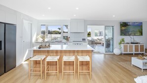 A modern kitchen with a large island, wooden bar stools, and a view of the outdoors. - Bohemian Coastal Dream (Port Macquarie)