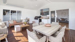 A spacious living area with a large dining table, wicker furniture, a sofa, and a television mounted on the wall. - Bohemian Coastal Dream (Port Macquarie)