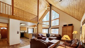 A spacious living area with a high ceiling, wooden beams, and large windows.