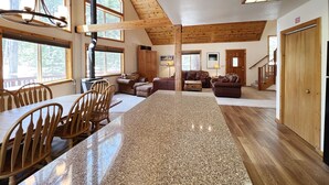 A spacious living area with a high ceiling, wooden beams, a fireplace, and large windows.