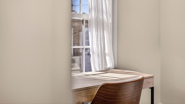 A room with a wooden desk and chair, a window with white curtains, and a view of a brick building outside. - Newly Built Carriage House in Unbeatable Location by Lucky Savannah (Savannah)