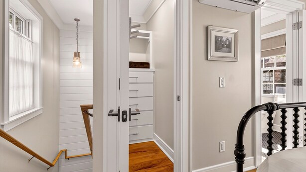 A hallway with a wooden staircase, a white closet with drawers, a hanging light fixture, and a framed picture on the wall. - Newly Built Carriage House in Unbeatable Location by Lucky Savannah (Savannah)