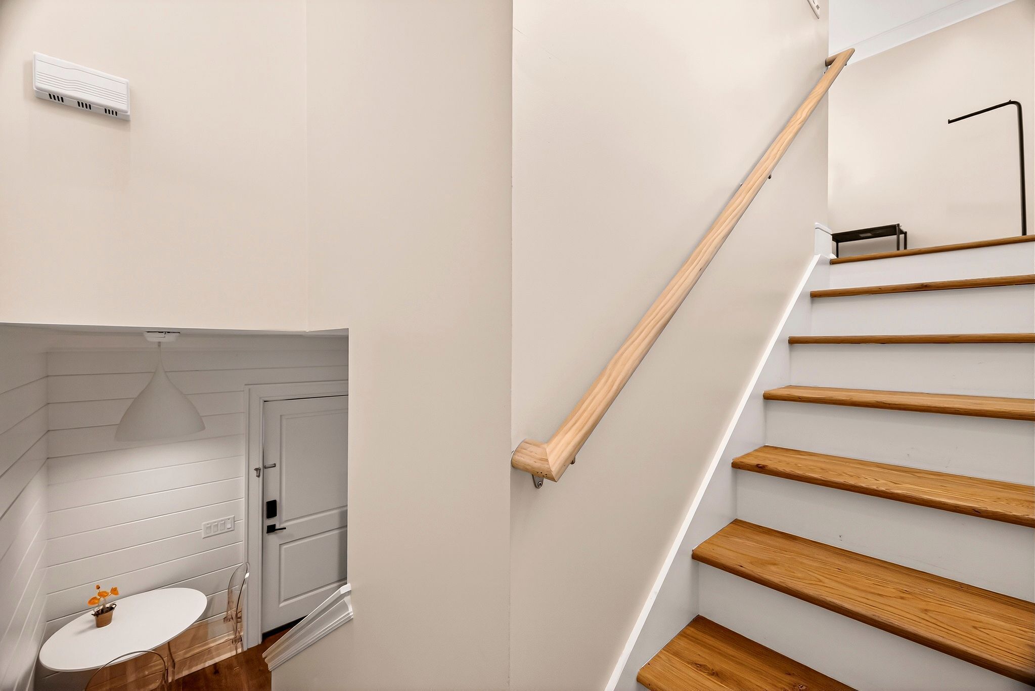 Een trap met houten treden en een leuning, die leidt naar een kamer met een witte deur en een kleine tafel met stoelen.