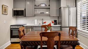 Una cocina con gabinetes grises, un refrigerador de acero inoxidable, un microondas y un horno. Hay una mesa de comedor con sillas y un florero con flores.