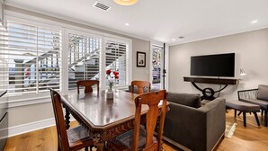 Una sala de estar moderna con comedor, que incluye una mesa de madera, sillas, un sofá y un televisor de pantalla plana montado en la pared.