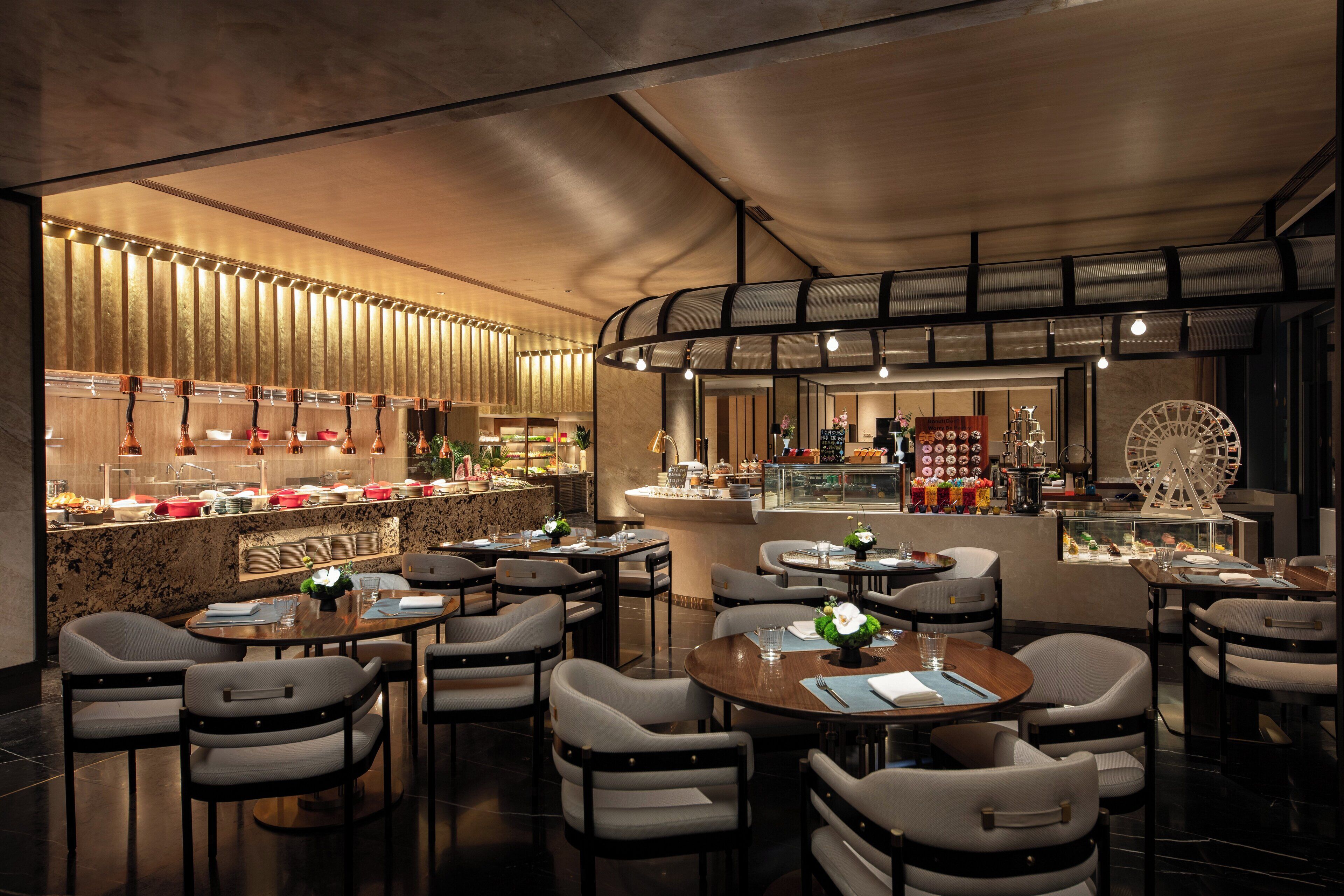 A modern restaurant interior with multiple dining tables and chairs, a bar area with a variety of food items, and a decorative wheel structure.