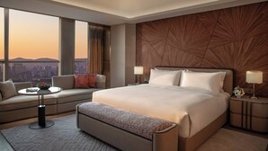 Una habitación de hotel moderna con una cama grande, un sofá, una mesita y vistas al horizonte de la ciudad.