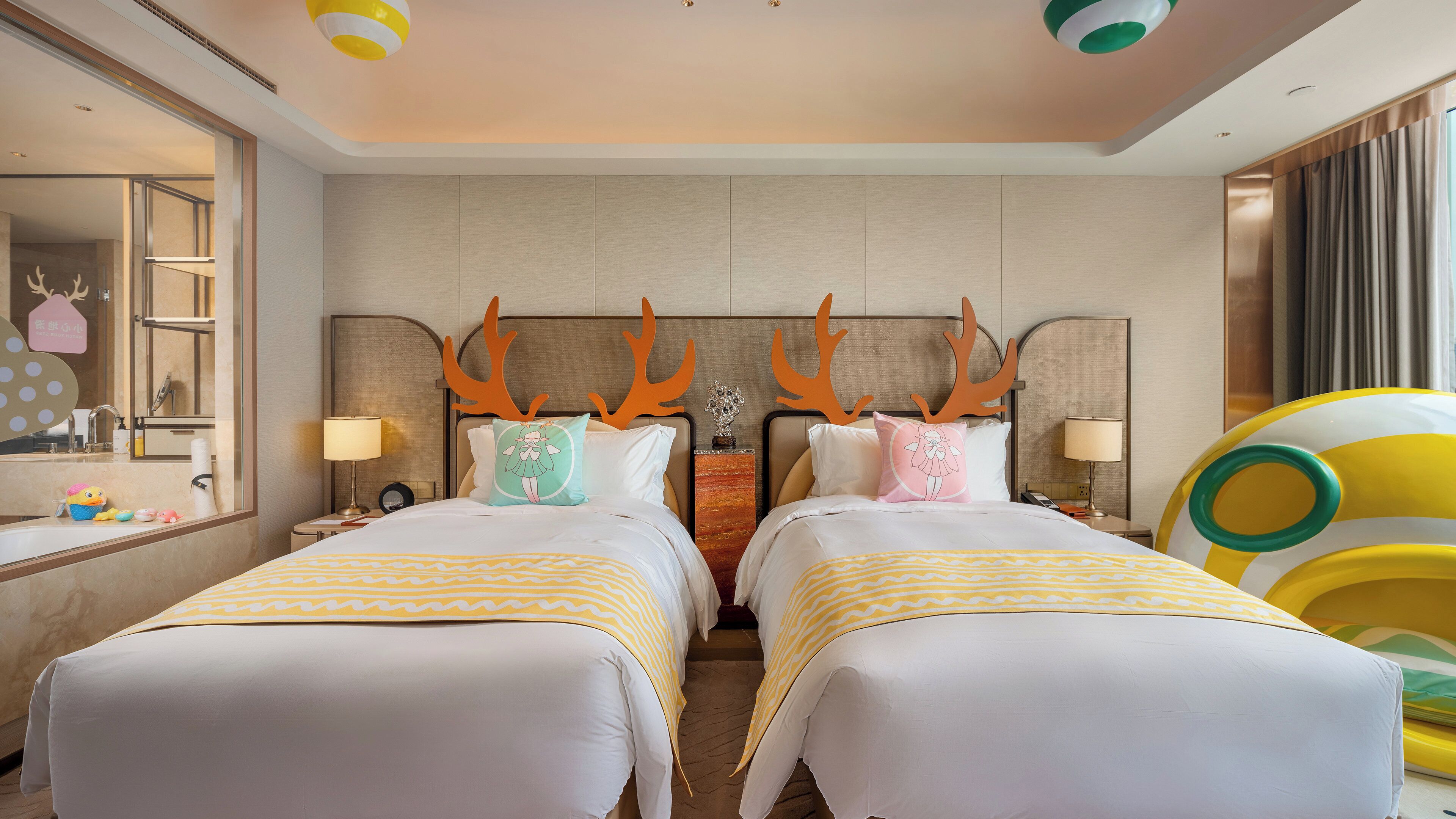 A hotel room with two beds, a large mirror, a bathroom with a sink and a toilet, and a window with curtains.