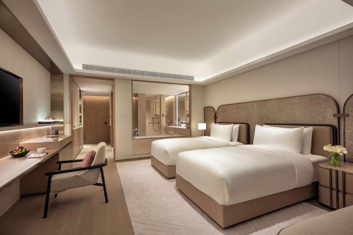 Een moderne hotelkamer met een groot bed, een bureau met stoel, een kaptafel met spiegel, en een badkamer die door een open deur zichtbaar is.
