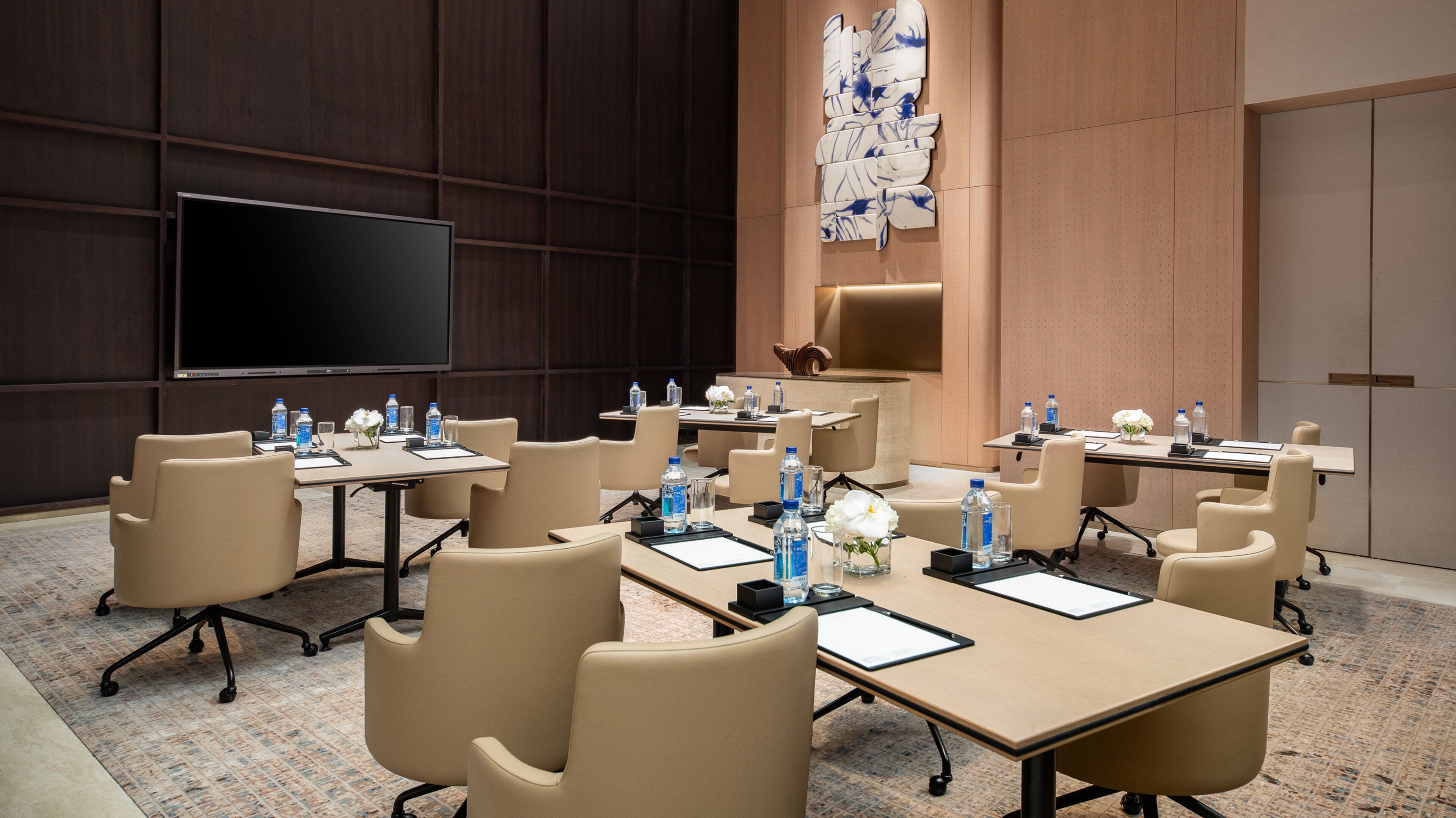 A conference room with multiple tables, chairs, and a large screen.