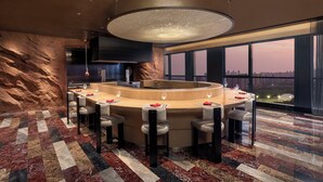 Un área de bar moderna con diseño circular, asientos y un ventanal con vistas a la ciudad.