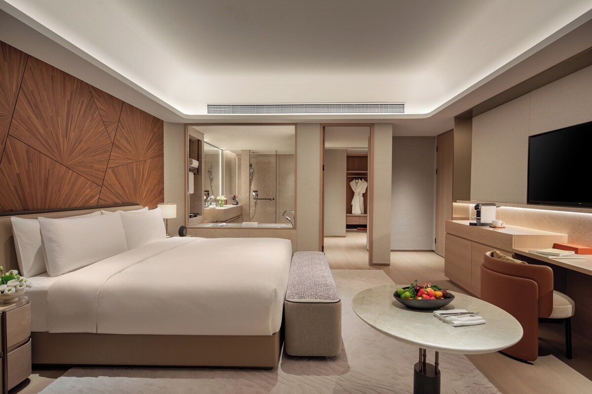 Een moderne hotelkamer met een groot bed, een bureau, een televisie en een badkamer zichtbaar door een geopende deur.