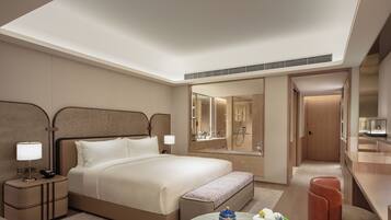 A modern hotel room with a large bed, bedside tables, a desk, and a bathroom visible through an open door.