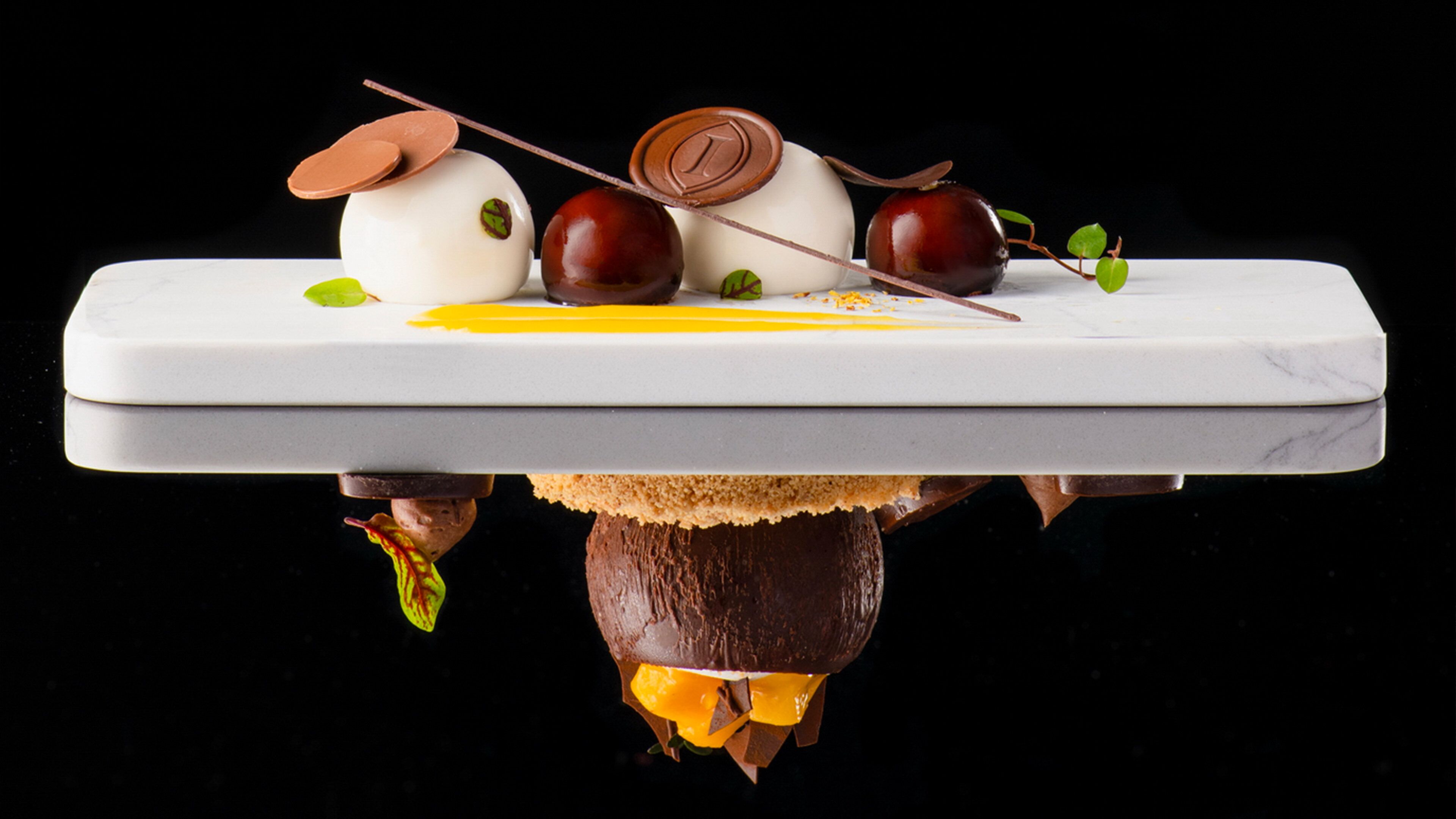 A dessert plate with various sweets and a chocolate piece on a white marble surface.