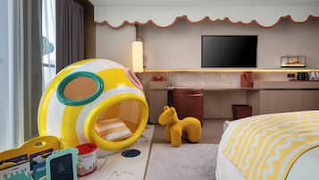 Habitación de hotel con zona de juegos, cama, televisor y minibar.