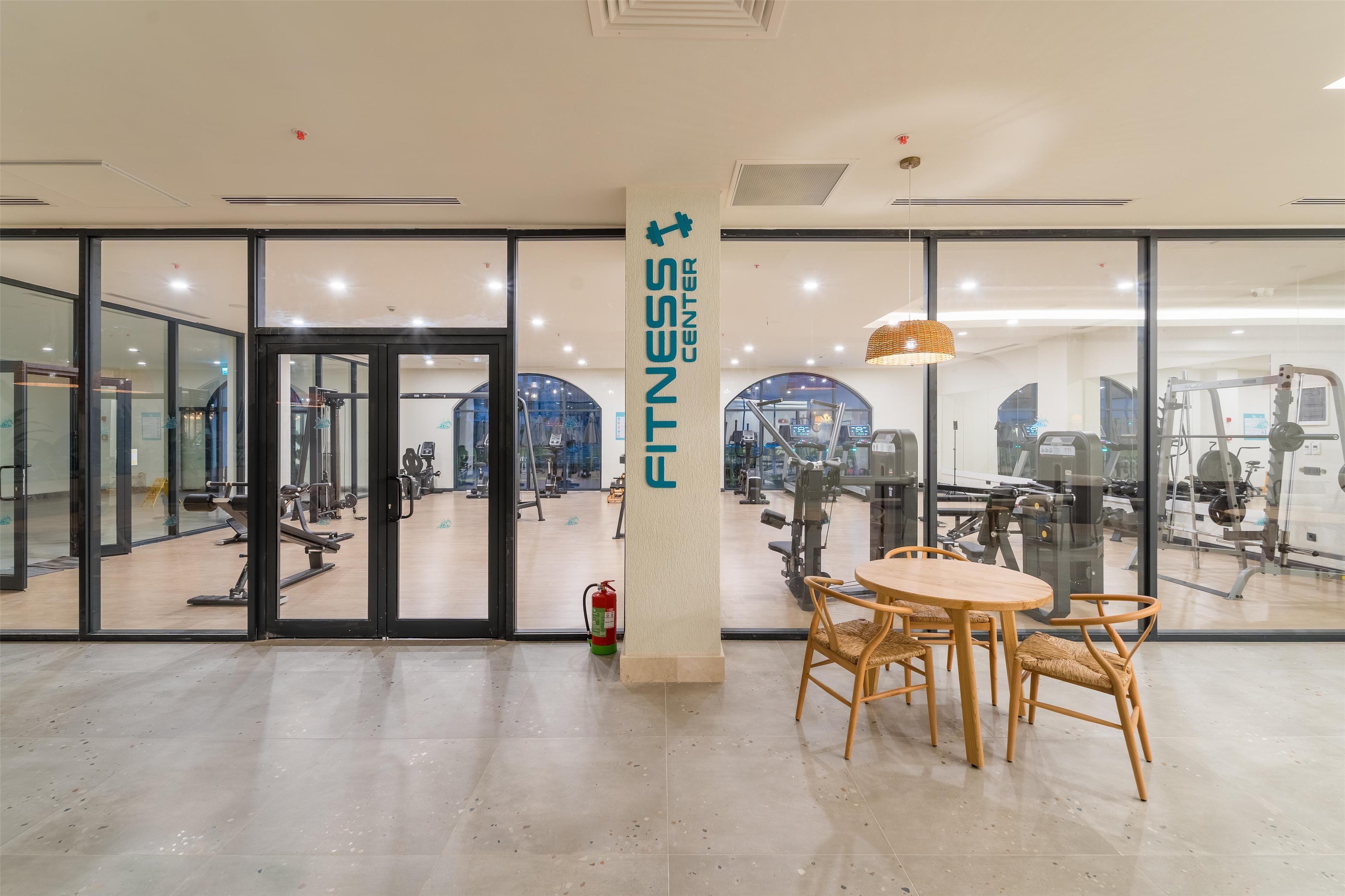 A gym with exercise equipment, a fire extinguisher, and a table with chairs in the center.