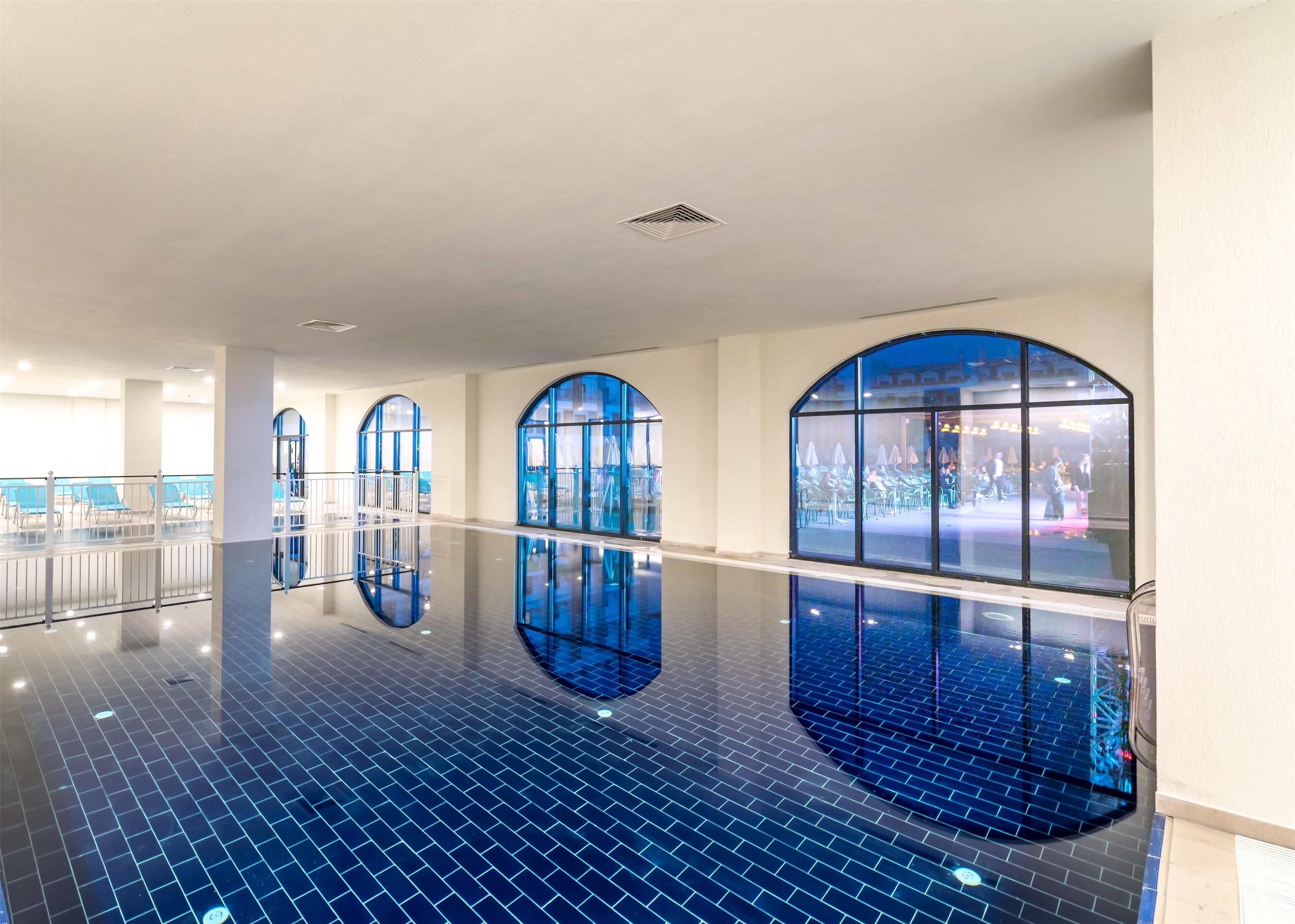 A spacious indoor area with a reflective tiled floor, large arched windows, and a view of an outdoor seating area.
