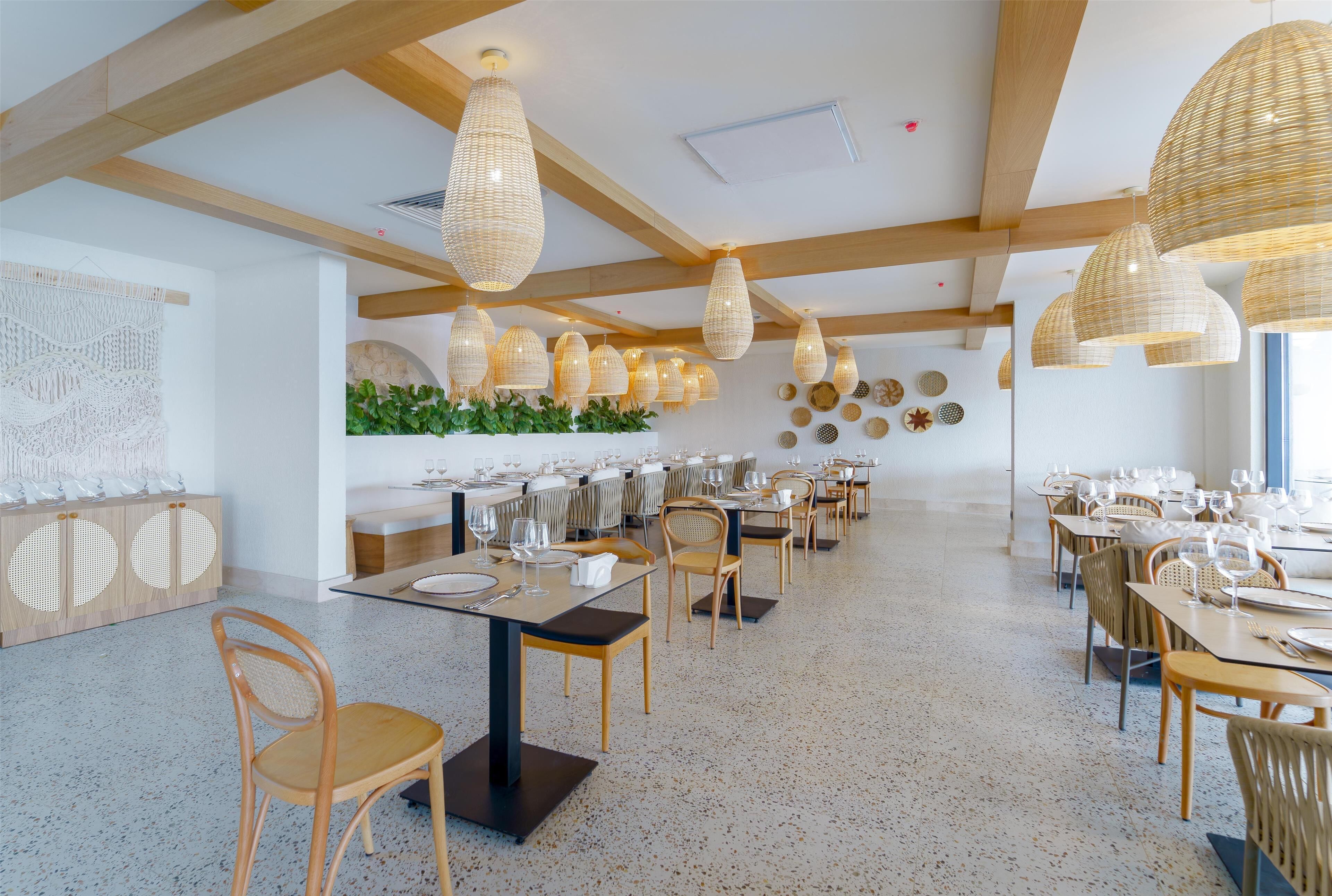A spacious dining area with high wooden beams, woven pendant lights, and a long table set for multiple guests.