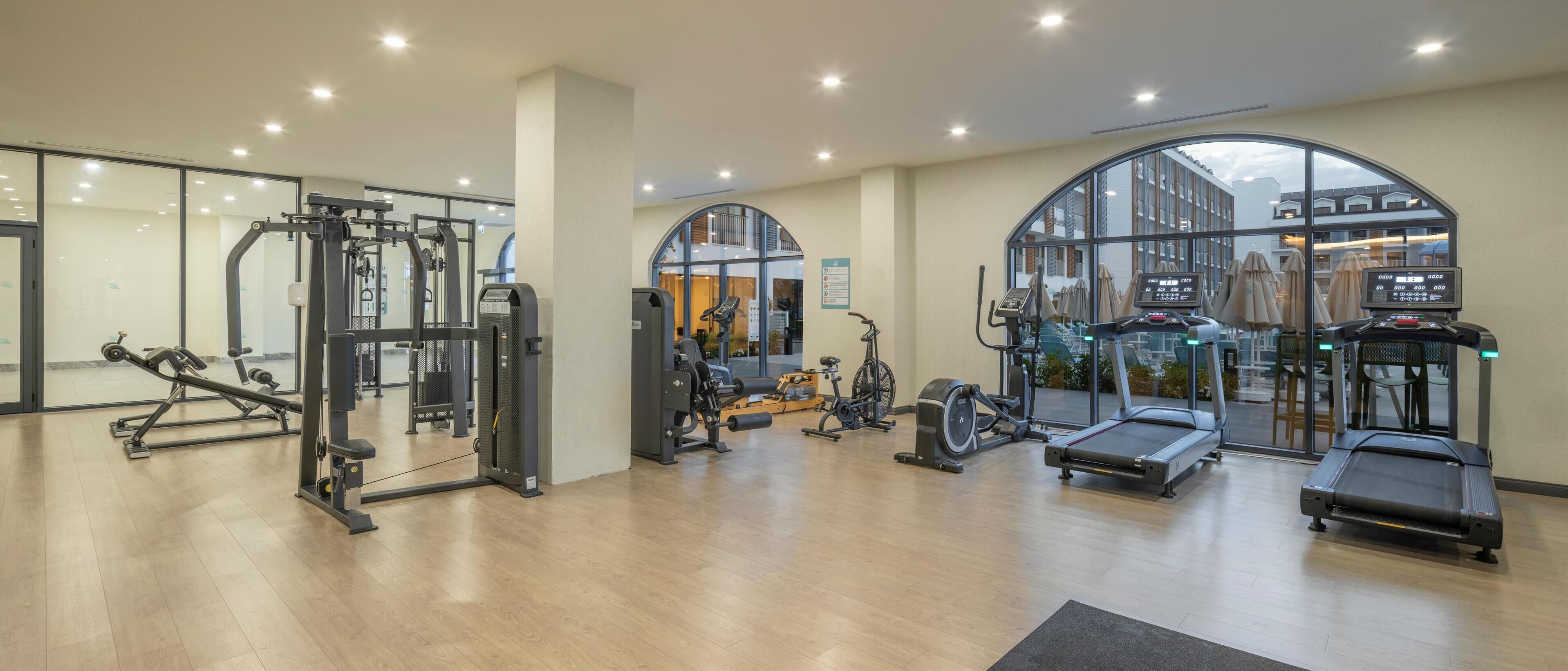 Een sportschool met diverse fitnessapparaten, grote ramen en een modern interieur.