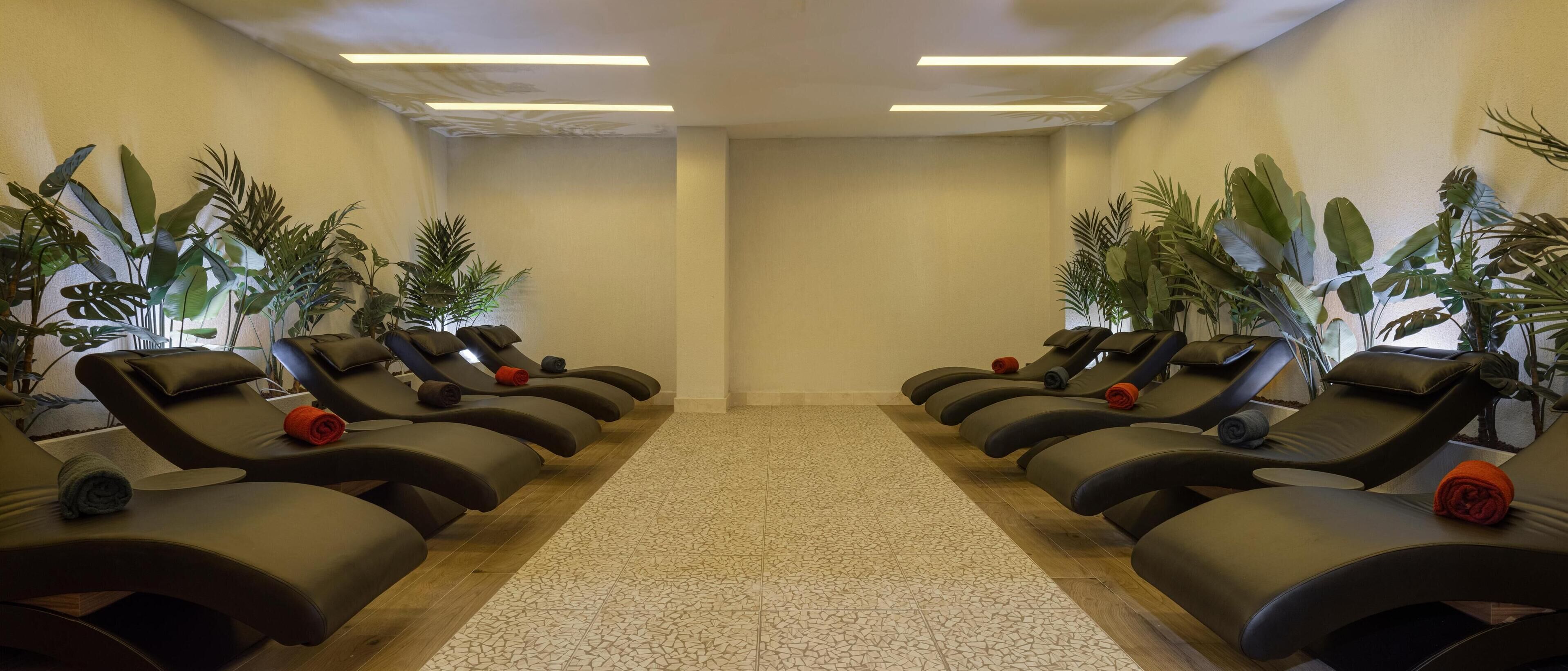 A room with multiple massage chairs arranged in two rows, each with a towel and a rolled-up item on the seat.