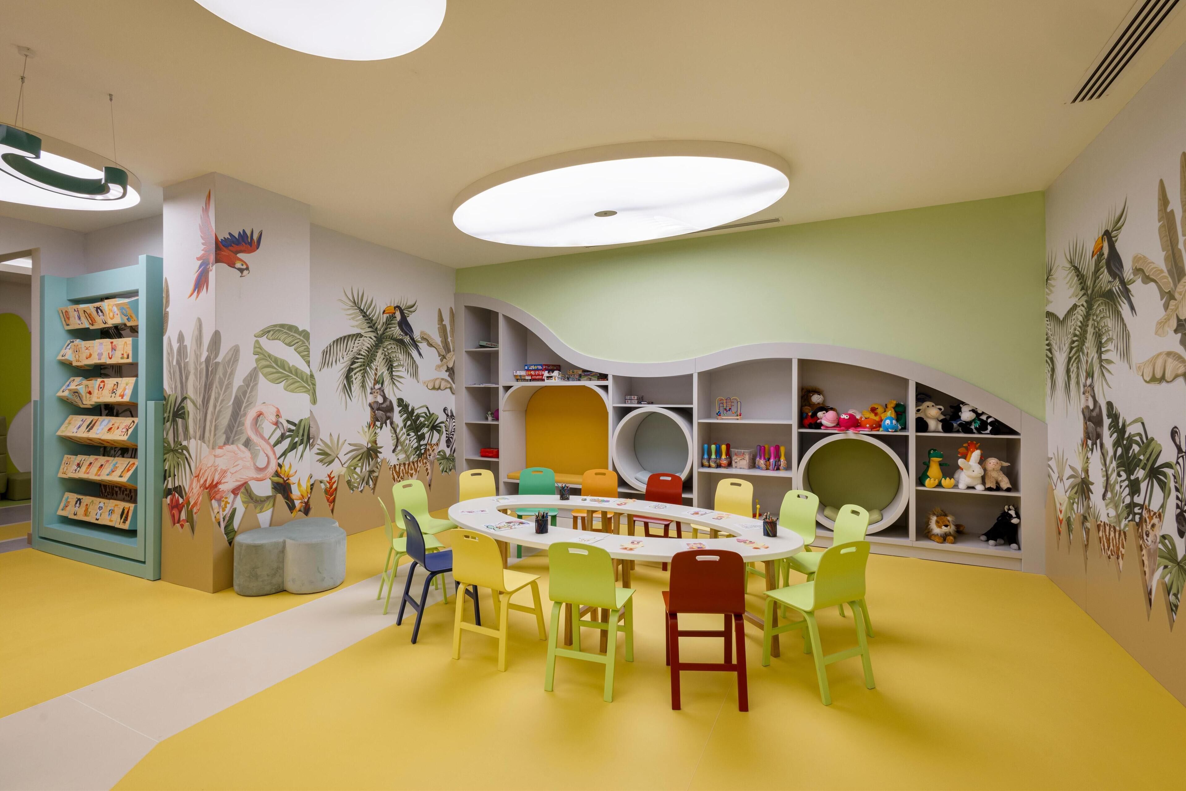 A children's playroom with a circular table, colorful chairs, and shelves with toys and books.