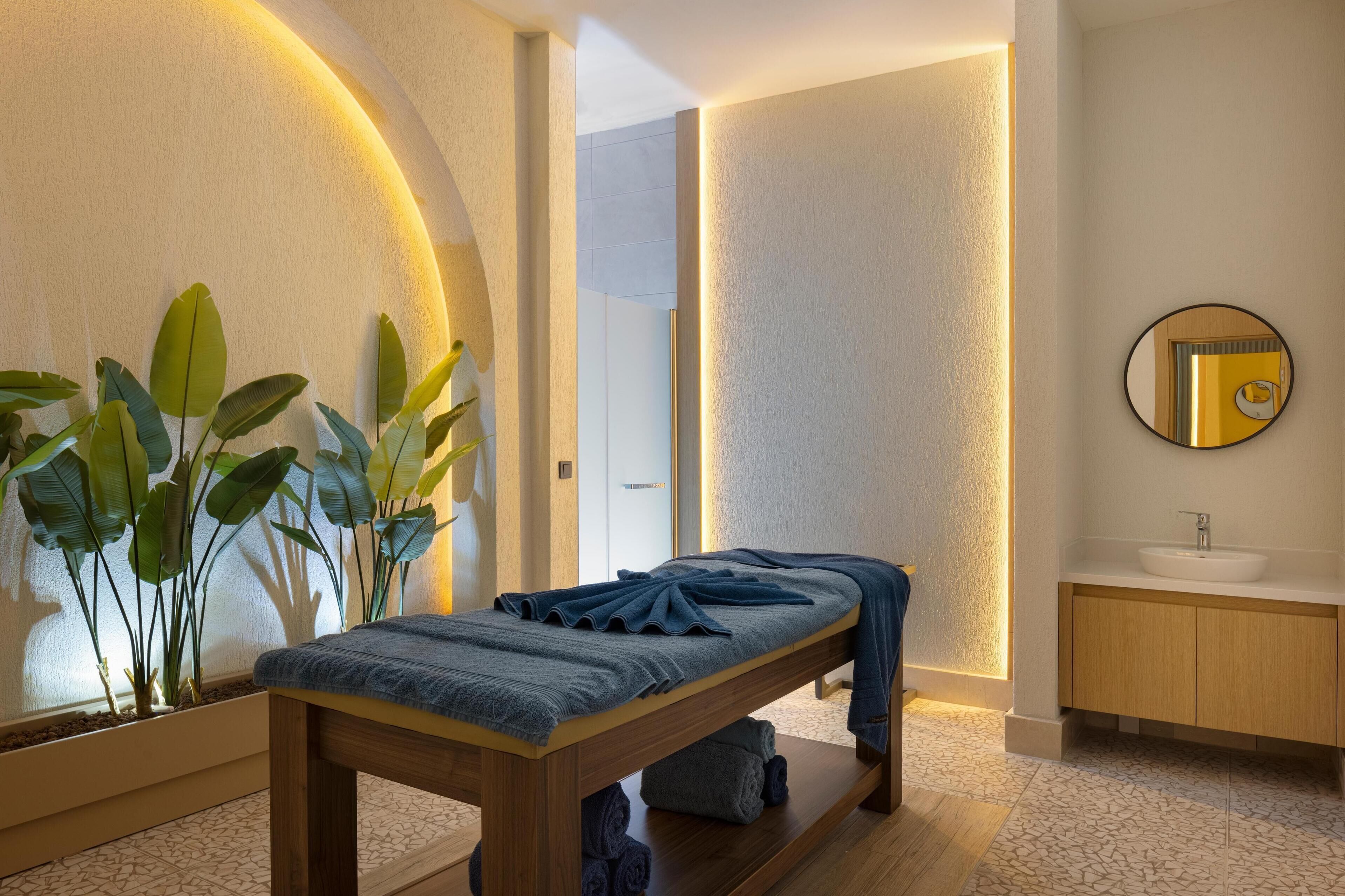 Ett modernt sparum med ett massageställ i trä, en stor spegel och ett träskåp med handfat.