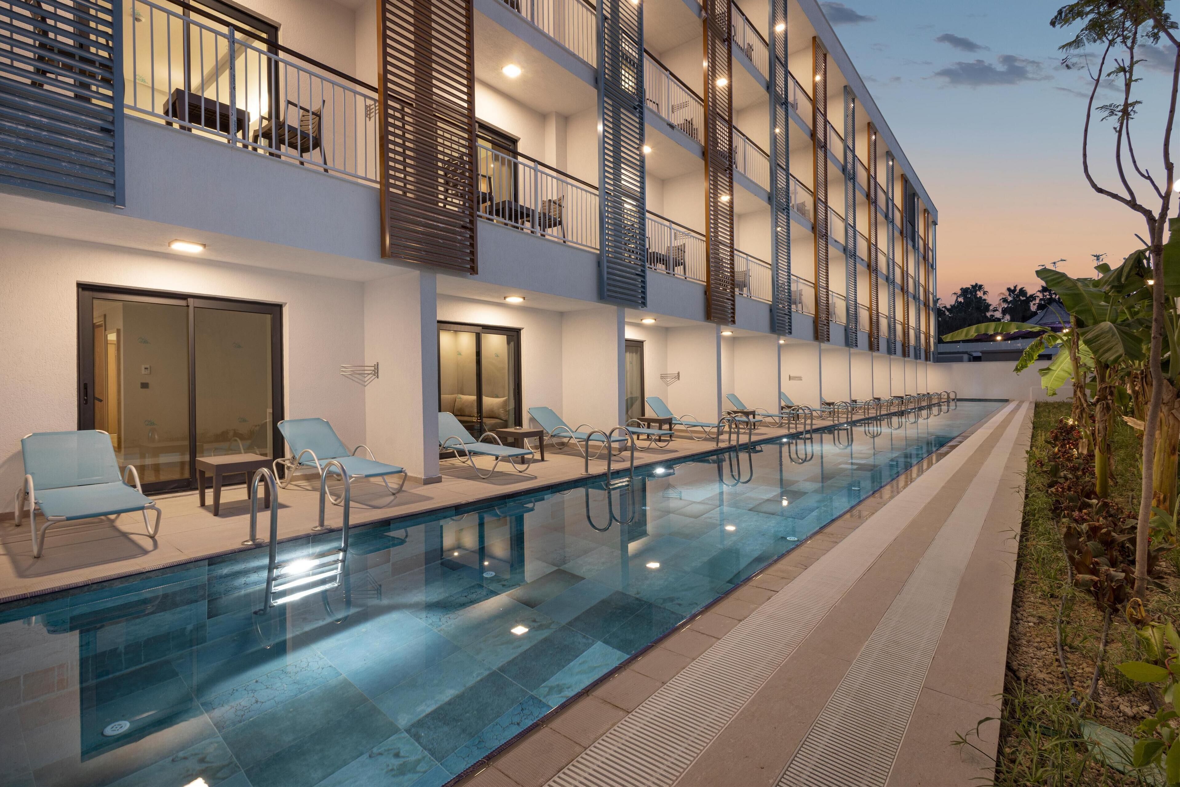 A modern hotel with a long swimming pool, multiple balconies, and sun loungers.