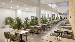 A spacious indoor dining area with multiple tables and chairs, large windows, and potted plants. - Arcanus Hotels Trendline Side (Manavgat)