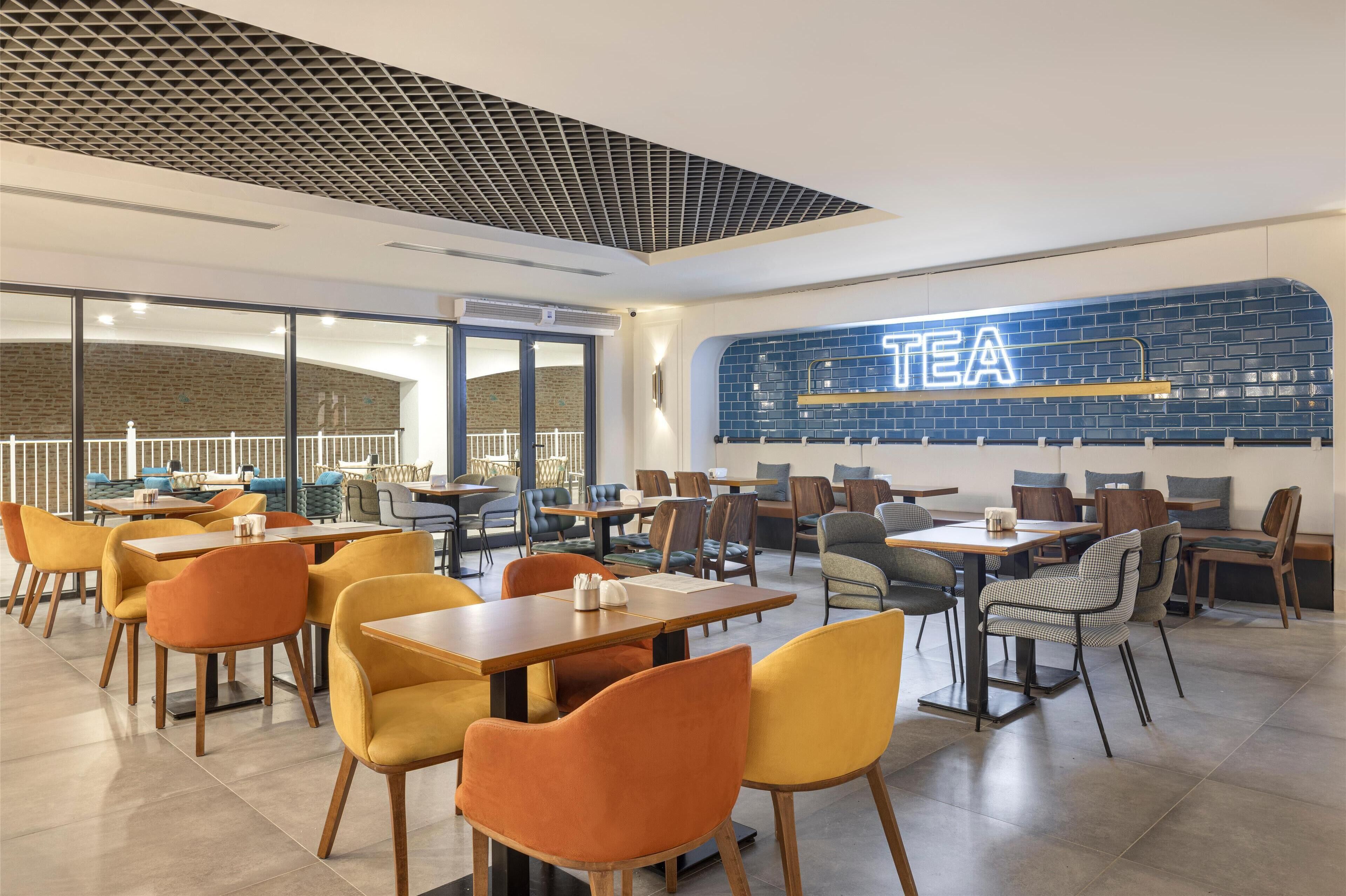 Un café moderne avec une enseigne bien visible indiquant « THÉ », des tables en bois et des chaises colorées.