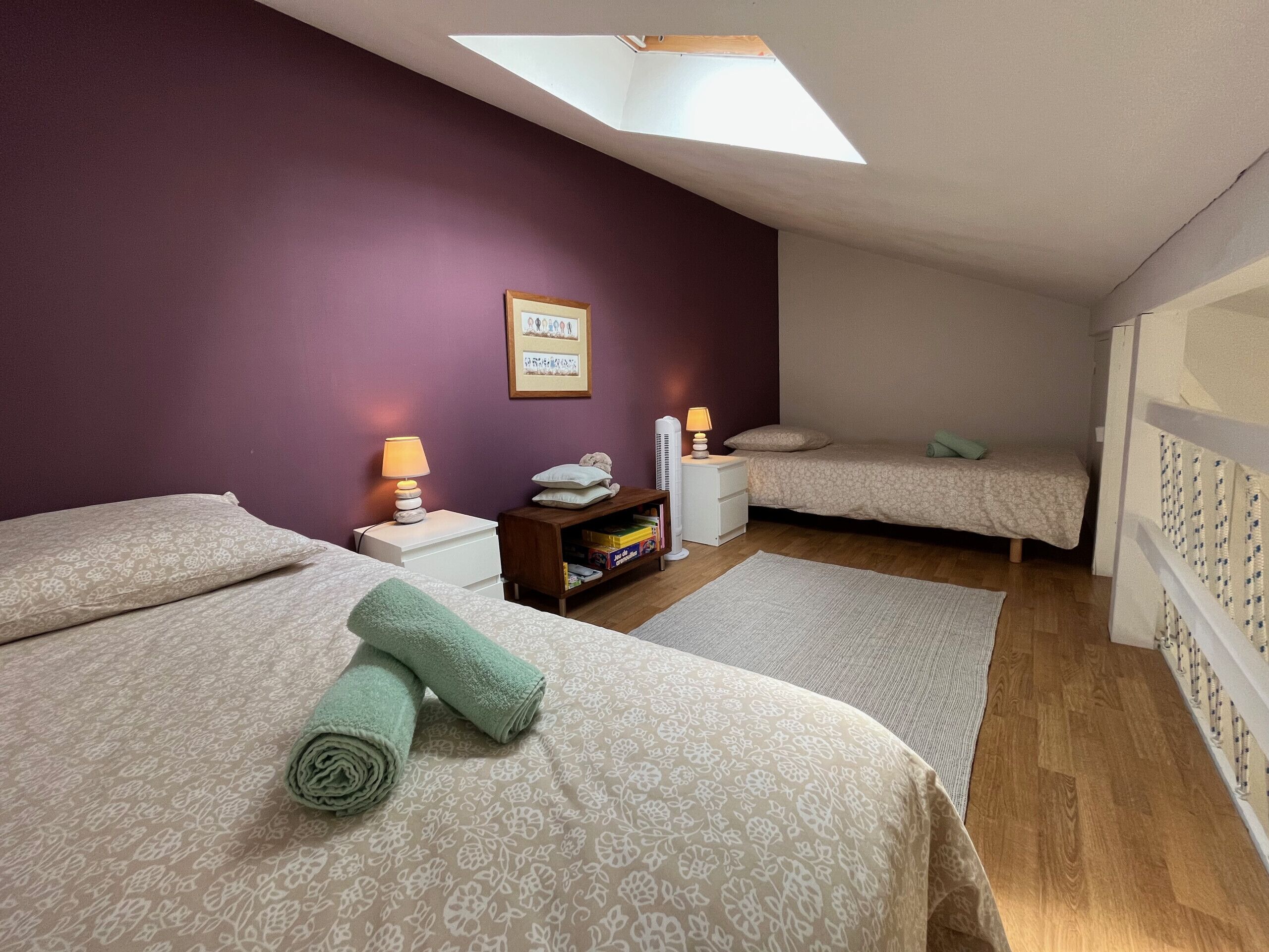 A bedroom with two beds, a skylight, a bedside table with lamps, and a nightstand with a lamp.