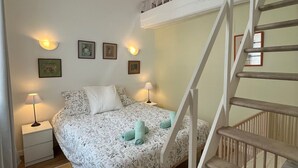 A bedroom with a bed, two bedside tables, a nightstand, a staircase, and a small balcony.